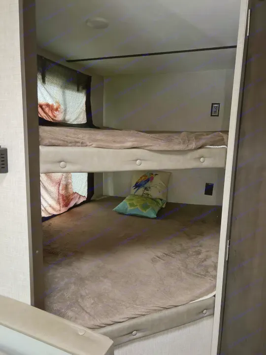 Cozy RV rental bunk beds: dimly lit sleeping area with two bunks, blankets, and decorative pillows inside a camper.. Keystone RV Bullet Crossfire 2019