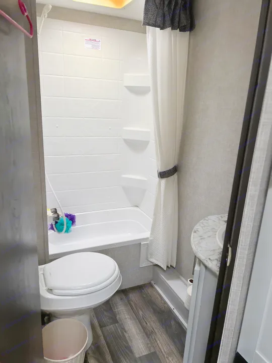 Compact rv rental bathroom with shower, toilet, and sink. Dark wood-look floor, white fixtures.. Keystone RV Bullet Crossfire 2019