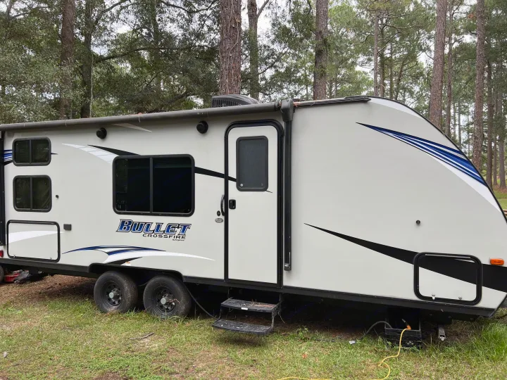 Keystone Bullet Crossfire travel trailer, an RV rental, parked outdoors among trees. Shows modern design & dual axles.. Keystone RV Bullet Crossfire 2019