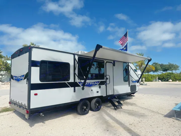 A white & black RV rental is parked on gravel with its awning out, under a blue sky & US flag.. Forest River Salem 2022