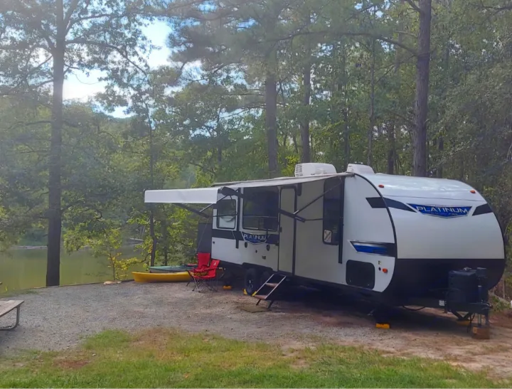 This RV rental is parked at a serene lakefront campsite, surrounded by lush trees, perfect for an outdoor getaway.. Forest River Salem 2022