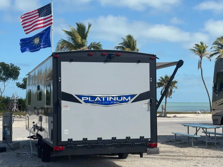 This RV is perfectly set up at a beautiful waterfront campsite with palm trees and flags, including a US flag. An ideal rv rental spot!. Forest River Salem 2022