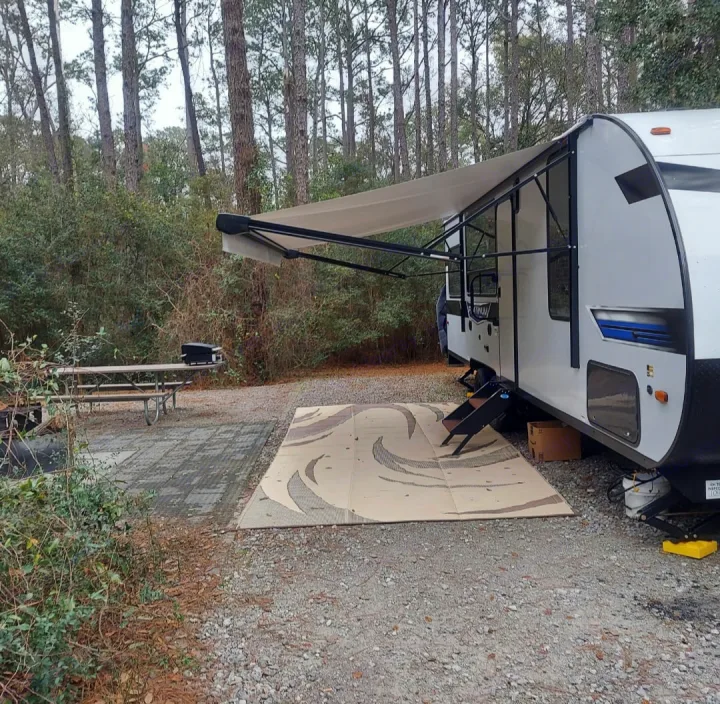 Relaxing at a wooded campsite with an RV rental, featuring an extended awning, outdoor mat, and picnic table.. Forest River Salem 2022