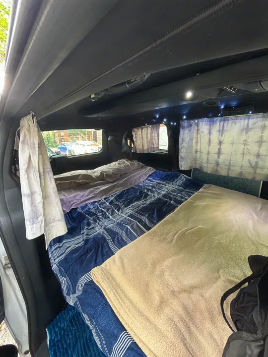 Cozy **rv rental** interior: a comfortable van sleeping setup with patterned bedding, privacy curtains, and string lights.. Dodge Dodge Grand Caravan GT 2017 2017