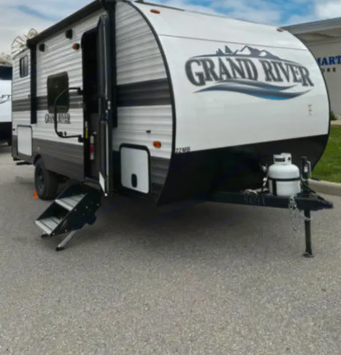 Grand River travel trailer RV rental parked on asphalt, with open door, steps, and front propane tank.. Gulf Stream Grand River 2024