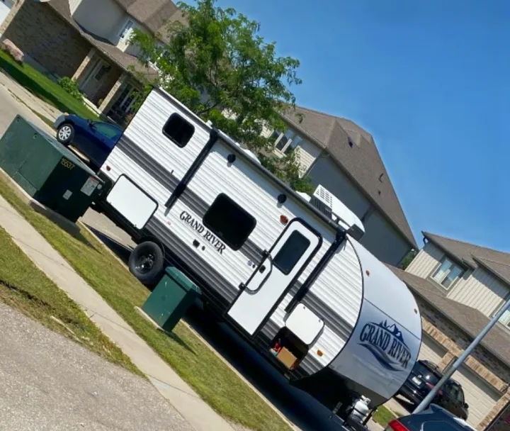 A white Grand River RV, a travel trailer, is parked on a sunny residential street, showcasing a great rv rental option.. Gulf Stream Grand River 2024