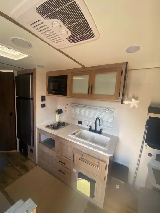 Inside this **rv rental**: a compact kitchen with an overhead AC unit, sink, stove, microwave, fridge, and wooden cabinets.. Gulf Stream Grand River 2024