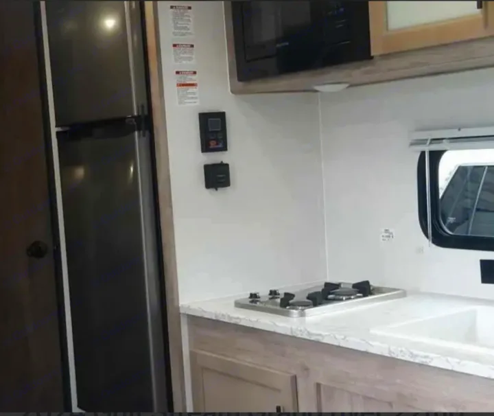 Explore this RV rental's modern kitchen featuring a fridge, built-in stove, sink, and overhead microwave.. Gulf Stream Grand River 2024