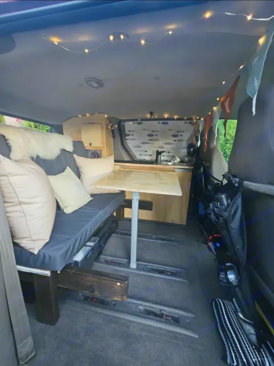 Cozy RV rental interior: minivan conversion with bench seating, portable table, compact kitchen, and string lights.. Dodge Caravan 2006