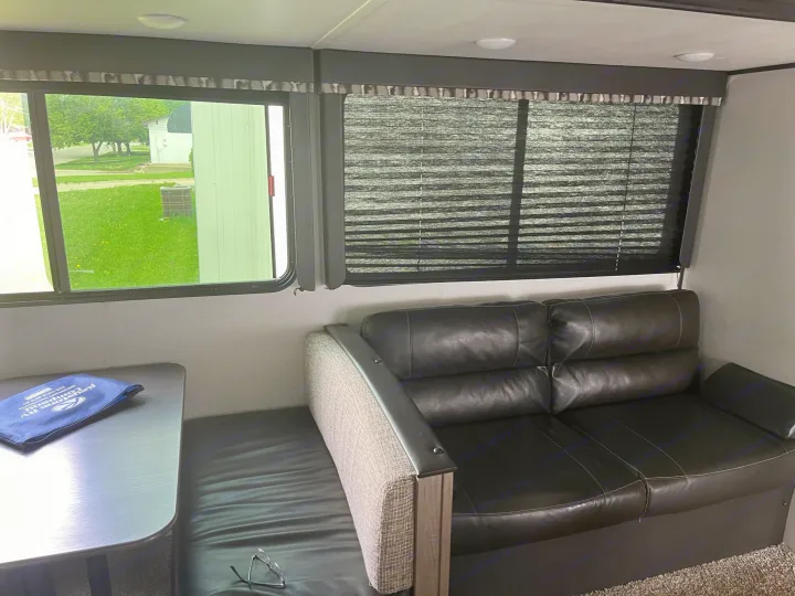 Explore this RV rental's inviting interior: a comfortable dark sofa, dining table, and windows with outdoor views & privacy blinds.. Keystone RV Hideout LHS 2020