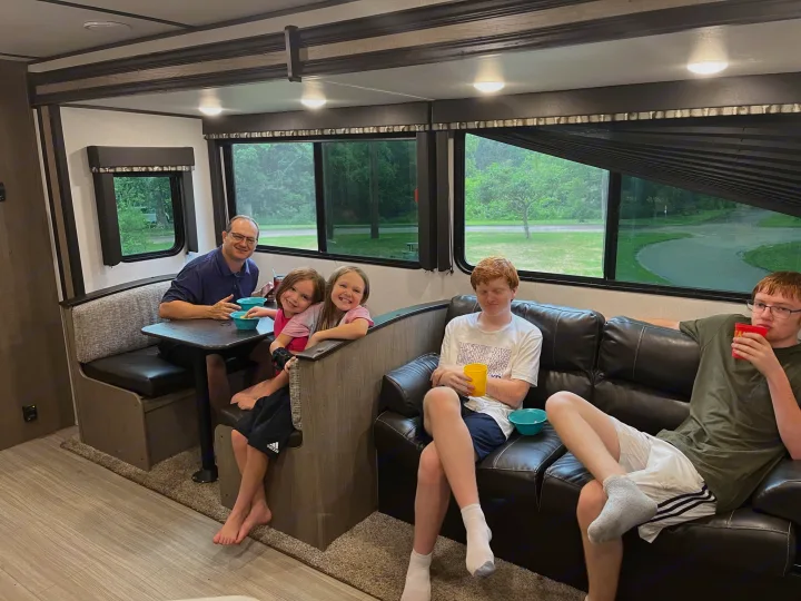 Comfortable RV rental interior: A family relaxes, some eating, with clear views of nature outside.. Keystone RV Hideout LHS 2020