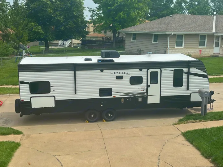 A large white and black Hideout travel trailer, ideal for an rv rental, parked on a residential driveway.. Keystone RV Hideout LHS 2020