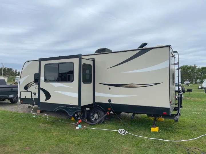 RV rental: Beige travel trailer with extended slide-out and utility hookups, parked on green grass at a campground.. Keystone RV Cougar 2018