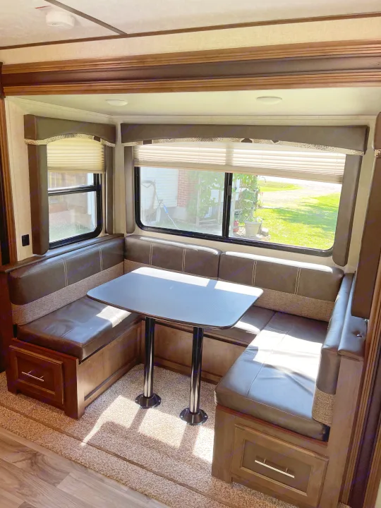 Comfortable U-shaped dinette in an RV rental, featuring a table, plush seating, and windows with outdoor views.. Keystone RV Cougar 2018