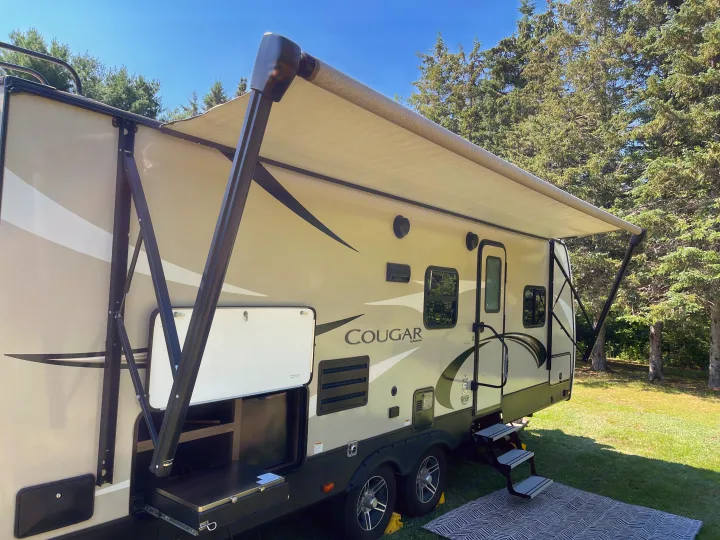 A Cougar RV rental with extended awning, outdoor kitchen, and steps on grass. Sunny day with trees.. Keystone RV Cougar 2018