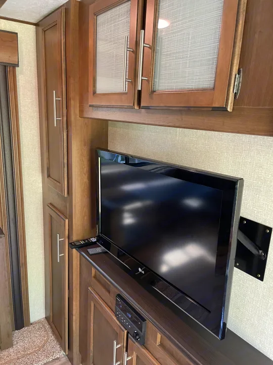 RV rental interior showcasing a mounted LG TV, integrated media player, and practical wooden cabinets for storage.. Keystone RV Cougar 2018