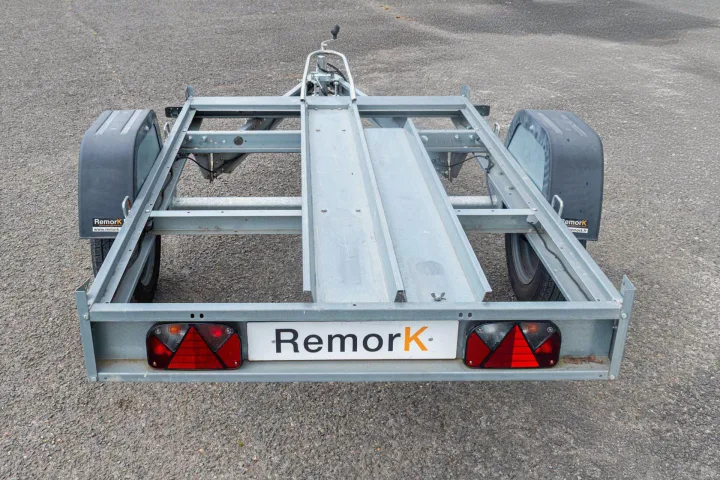 Empty grey metal motorcycle trailer, ideal for RV rental transport. Features two wheel tracks, fenders, & taillights.. RemorK Porte Moto 2025