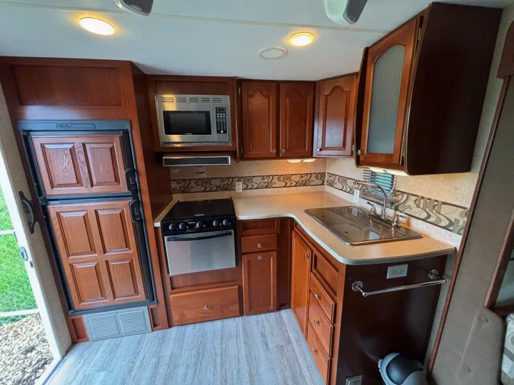 Well-equipped RV rental kitchen featuring wood cabinets, microwave, stove, sink, and refrigerator for comfortable travels.. Fleetwood 230RKS 2009