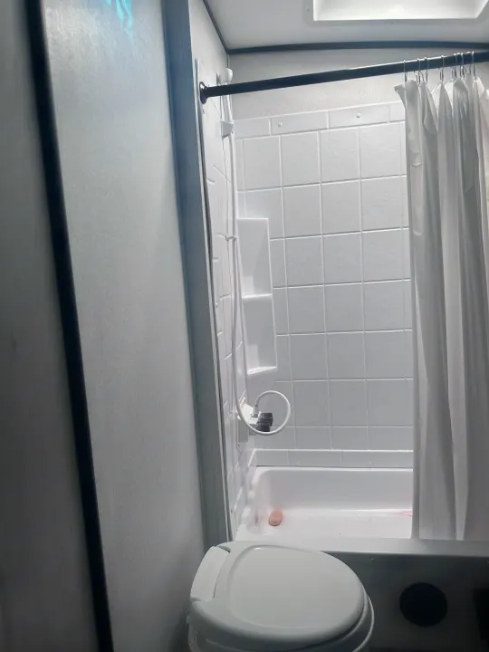 RV rental's compact bathroom features a white shower/tub, toilet, and tiled walls with a white shower curtain.. MPG Cruiser RV ultra light 2500 2021