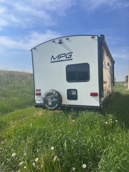 Rear view of a white MPG travel trailer rv rental parked in a tall grassy field under a bright blue sky.. MPG Cruiser RV ultra light 2500 2021