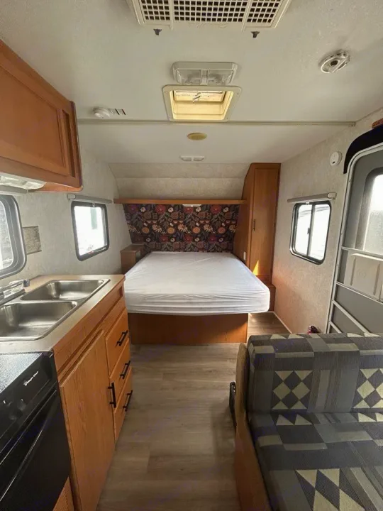This RV rental interior features a rear bed with a floral headboard, kitchen with double sinks, and a patterned sofa.. Terry Dakota 722F 2004