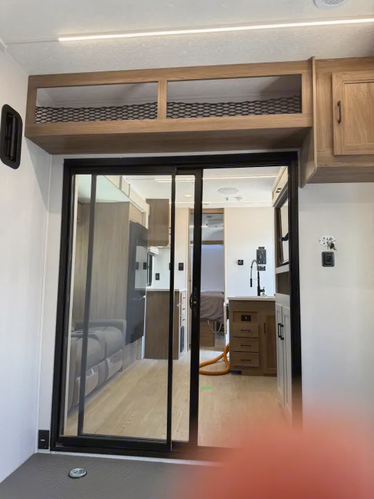 Spacious RV rental interior: sliding door reveals living, kitchen, and bedroom areas. Plus overhead storage.. Coachmen Adrenaline 2025