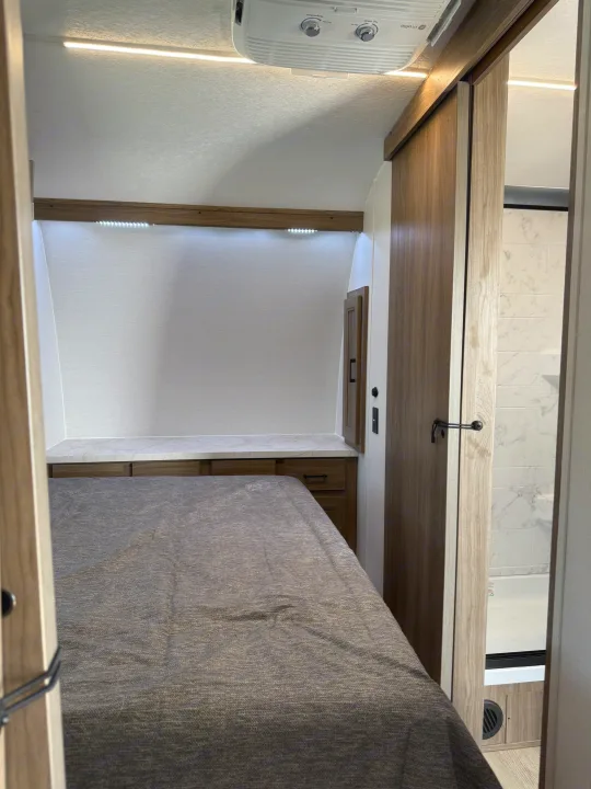 Cozy RV rental bedroom featuring a full bed, built-in storage, bright lighting, and an adjacent modern bathroom.. Coachmen Adrenaline 2025