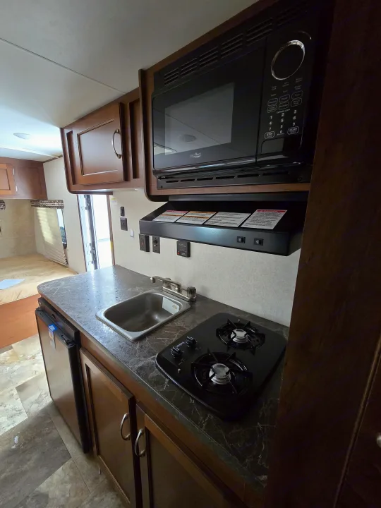 Compact RV rental kitchen featuring a microwave, two-burner stove, sink, and refrigerator. Ideal for mobile living.. Jayco Jay Flight SLX 2017
