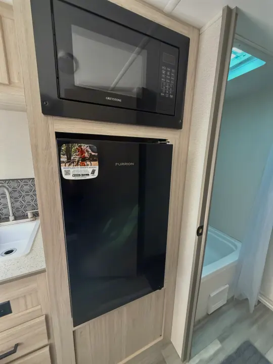 Compact RV rental interior showing a Greystone microwave, Furrion refrigerator, kitchen area, and a built-in bathroom.. Heartland Pioneer 2025
