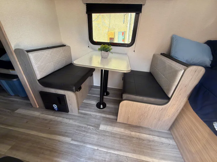 Compact RV rental dinette and bed area with modern wood-look interior, comfy seating, and table.. Heartland Pioneer 2025