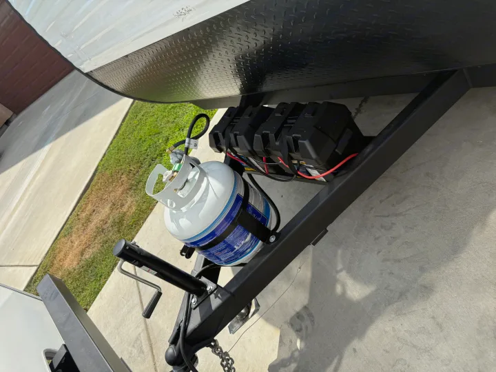 Front of an RV rental showing a white propane tank and black battery bank mounted on the trailer tongue.. Heartland Pioneer 2025