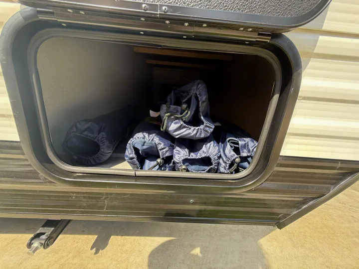 Open RV rental storage bay, revealing blue drawstring bags and various camping supplies inside.. Heartland Pioneer 2025