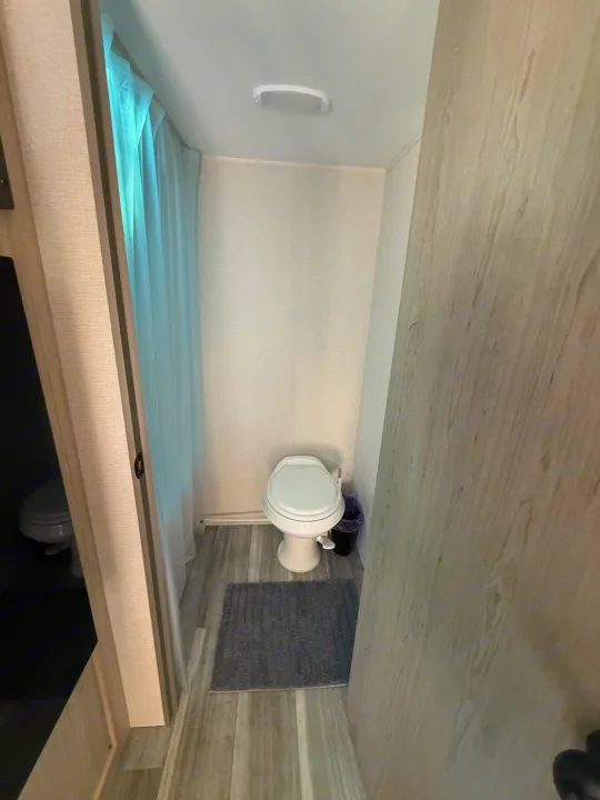 Compact RV rental bathroom, featuring a white toilet, gray rug, and a shower curtain on the left.. Heartland Pioneer 2025