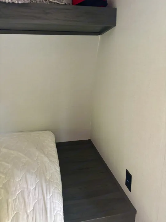 Inside an RV rental: a compact bedroom with a white mattress, overhead shelf, and wall charging port.. Dutchman Aspen Trail 2025