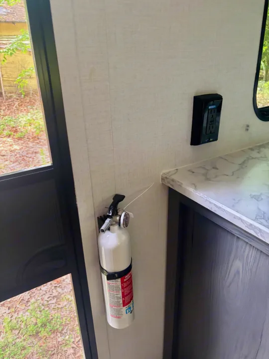 RV rental interior with a wall-mounted fire extinguisher, electrical outlet, and marbled countertop, ensuring safety.. Dutchman Aspen Trail 2025