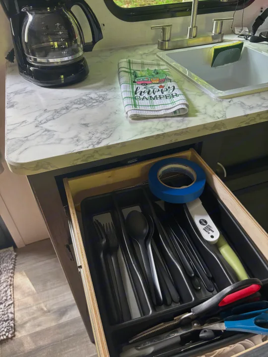 RV rental kitchen: coffee maker, sink with sponge, "Happy Camper" towel, and organized utensils in an open drawer.. Dutchman Aspen Trail 2025