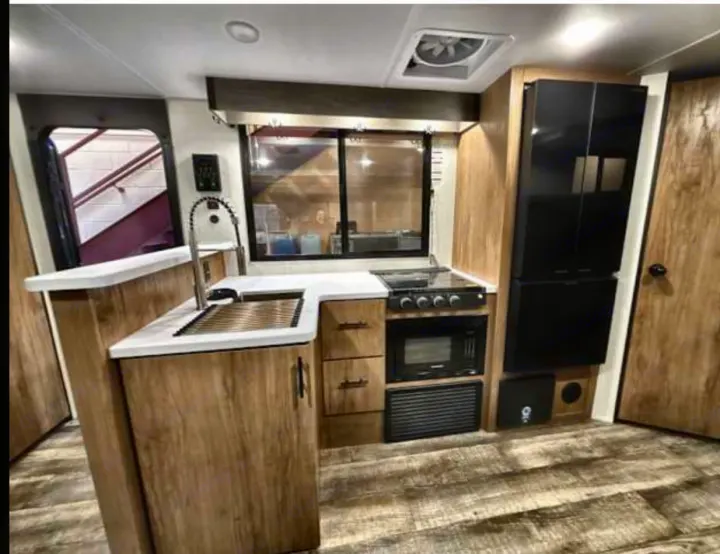 Modern RV rental kitchen with black fridge, stove, microwave, and wood cabinetry. Ready for your adventure.. Forest River Campsite Reserve 26CJ 2025
