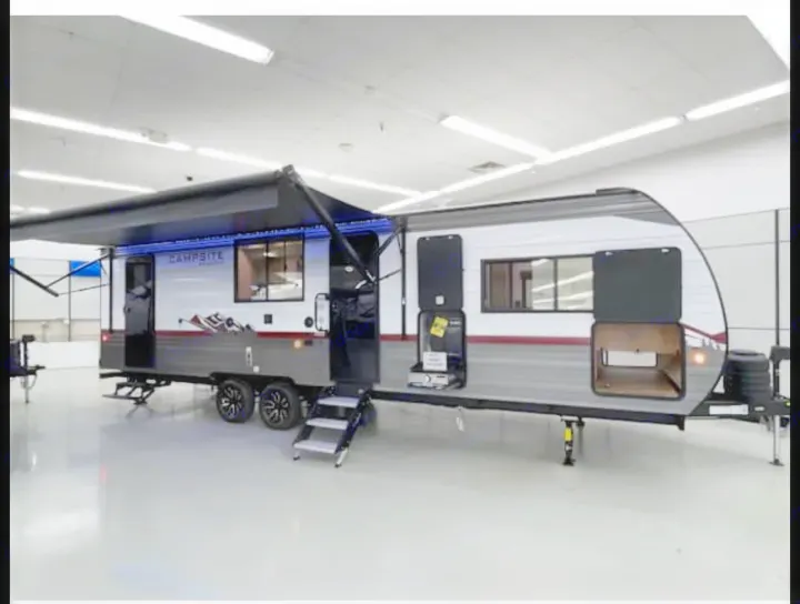 This Campsite travel trailer, ideal for RV rental, displays its extended awning with blue LEDs, steps, & open storage.. Forest River Campsite Reserve 26CJ 2025