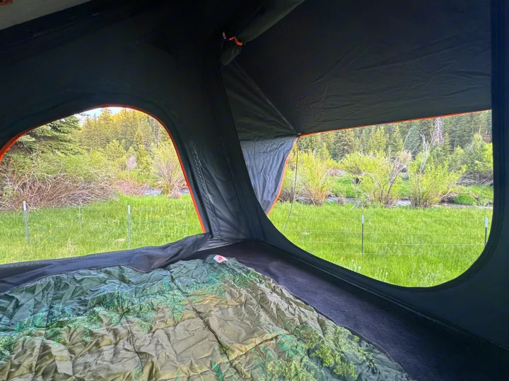 Cozy RV rental view from inside a rooftop tent, showing a sleeping bag and a scenic vista of green fields, river, & forest.. Toyota 4Runner 2020