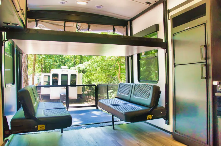Modern RV rental interior featuring a bunk bed, versatile seating, and an open rear patio with a serene wooded view.. Cruiser Stryker 2022