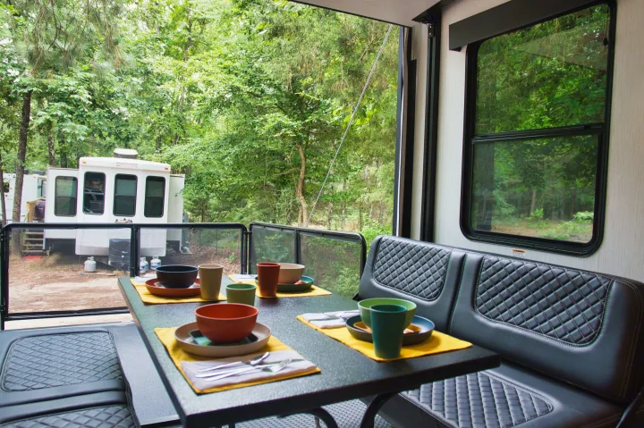Inside an RV rental: a set dining table with quilted seats, offering forest views and another RV at the campsite.. Cruiser Stryker 2022