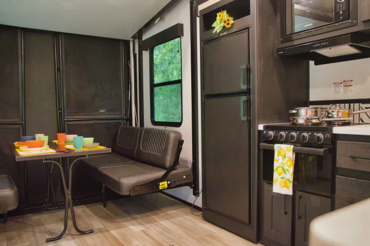 Modern RV rental interior with a well-equipped kitchen and dining area, featuring a stove, microwave, fridge, and wall-mounted bench.. Cruiser Stryker 2022
