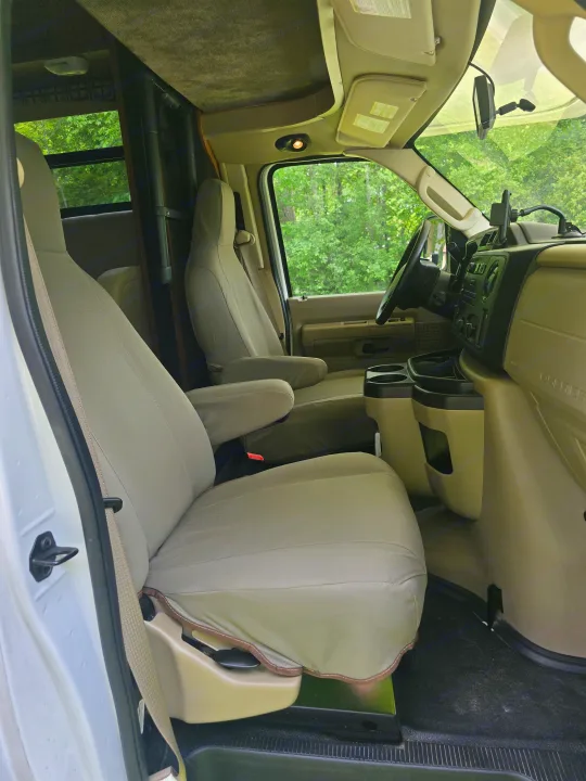 View inside an RV rental's front cabin showing comfortable seats, dashboard, and windows looking out to green trees.. Jayco Redhawk 2017