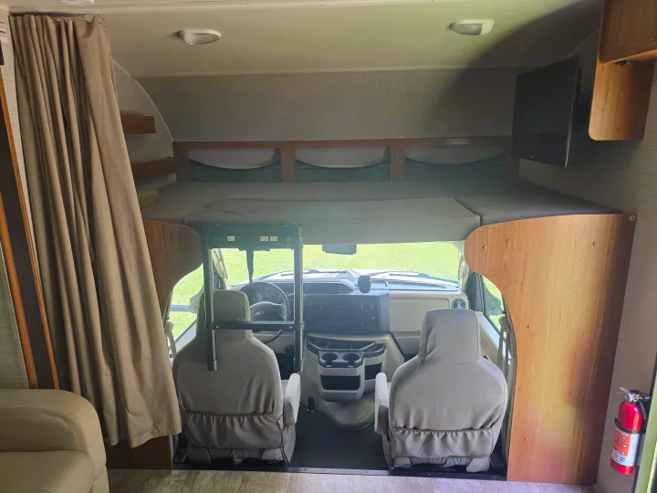 This RV rental interior features an over-cab sleeping area, cockpit with driver/passenger seats, a TV, and curtains.. Jayco Redhawk 2017