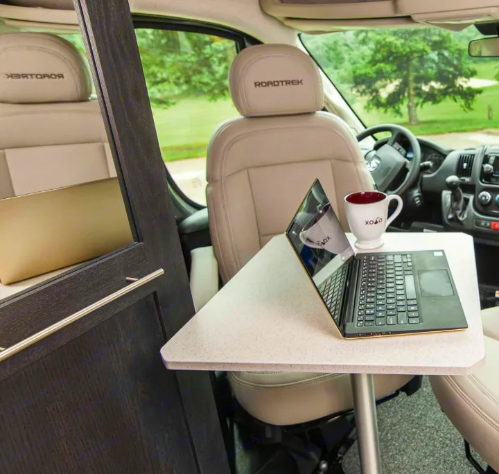 Work on the road! This RV rental offers a cozy mobile office with "ROADTREK" seats, a laptop, and a mug on a table.. Roadtrek Roadtrek Class B 2021