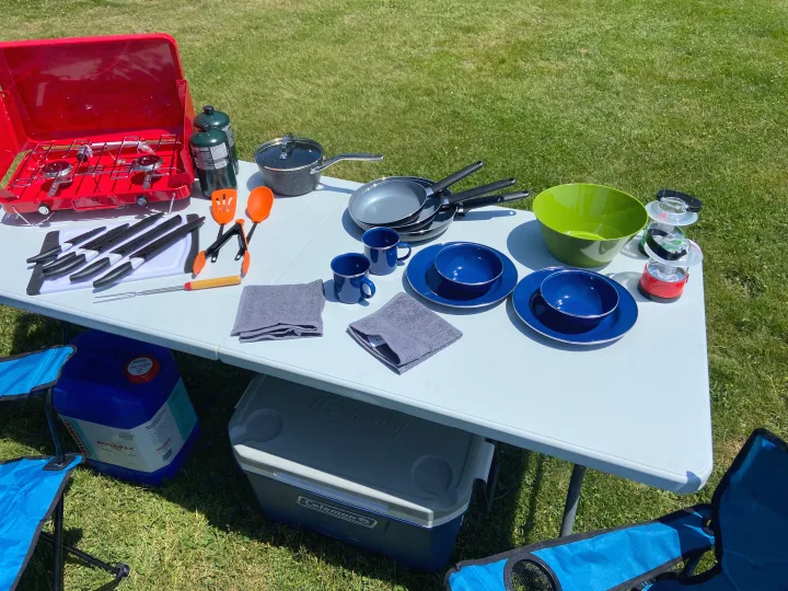 Complete outdoor cooking setup for your RV rental: a portable stove, various pans, blue dinnerware, and camping gear on a table.. Dodge Grand Caravan 2008