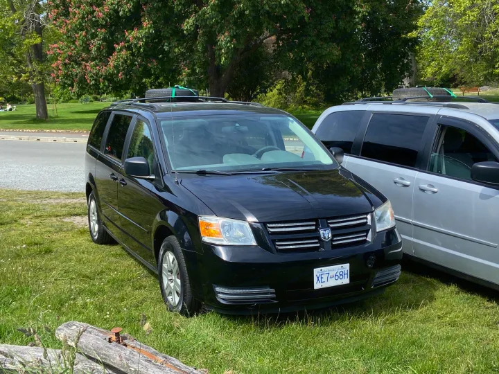 Black minivan & silver van parked on grass, equipped for travel like an RV rental for road trips.. Dodge Grand Caravan 2008