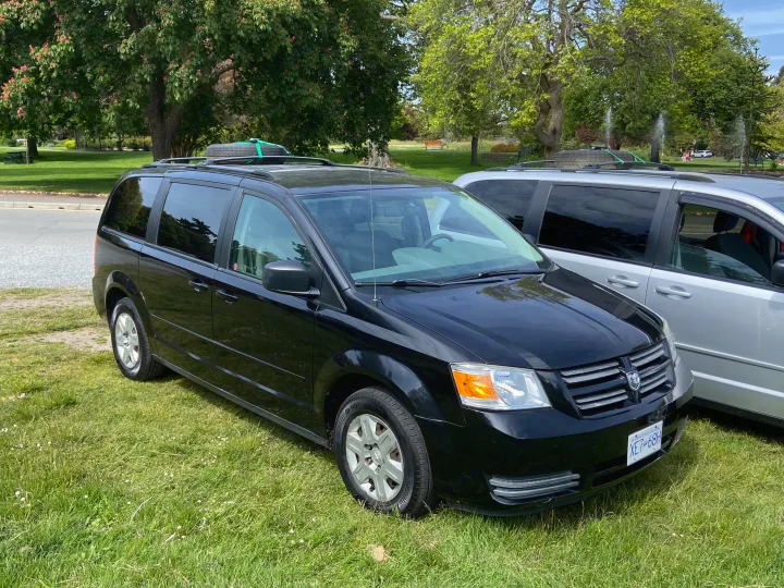 Two minivans, ideal for an RV rental alternative, parked on lush grass in a scenic park. Great for budget travel.. Dodge Grand Caravan 2008