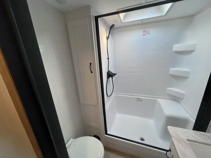 Experience comfort in this RV rental bathroom: a clean shower/tub, black fixtures, toilet, & compact storage.. Forest river 306RKTS Palomino 2025