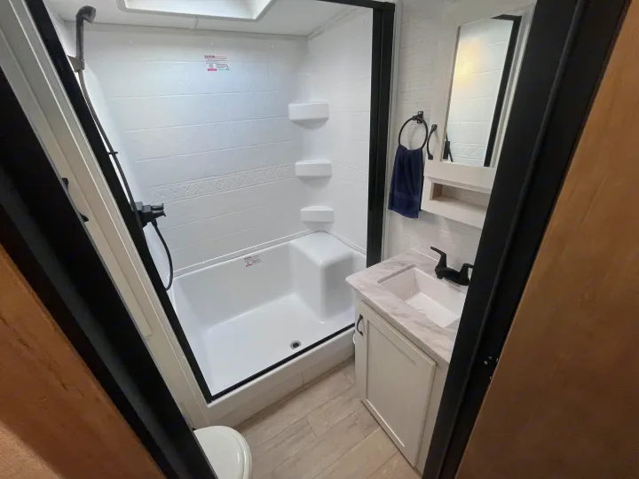 RV rental: Clean, modern bathroom with a white shower, dark fixtures, vanity sink, mirror, and light wood-look floor.. Forest river 306RKTS Palomino 2025